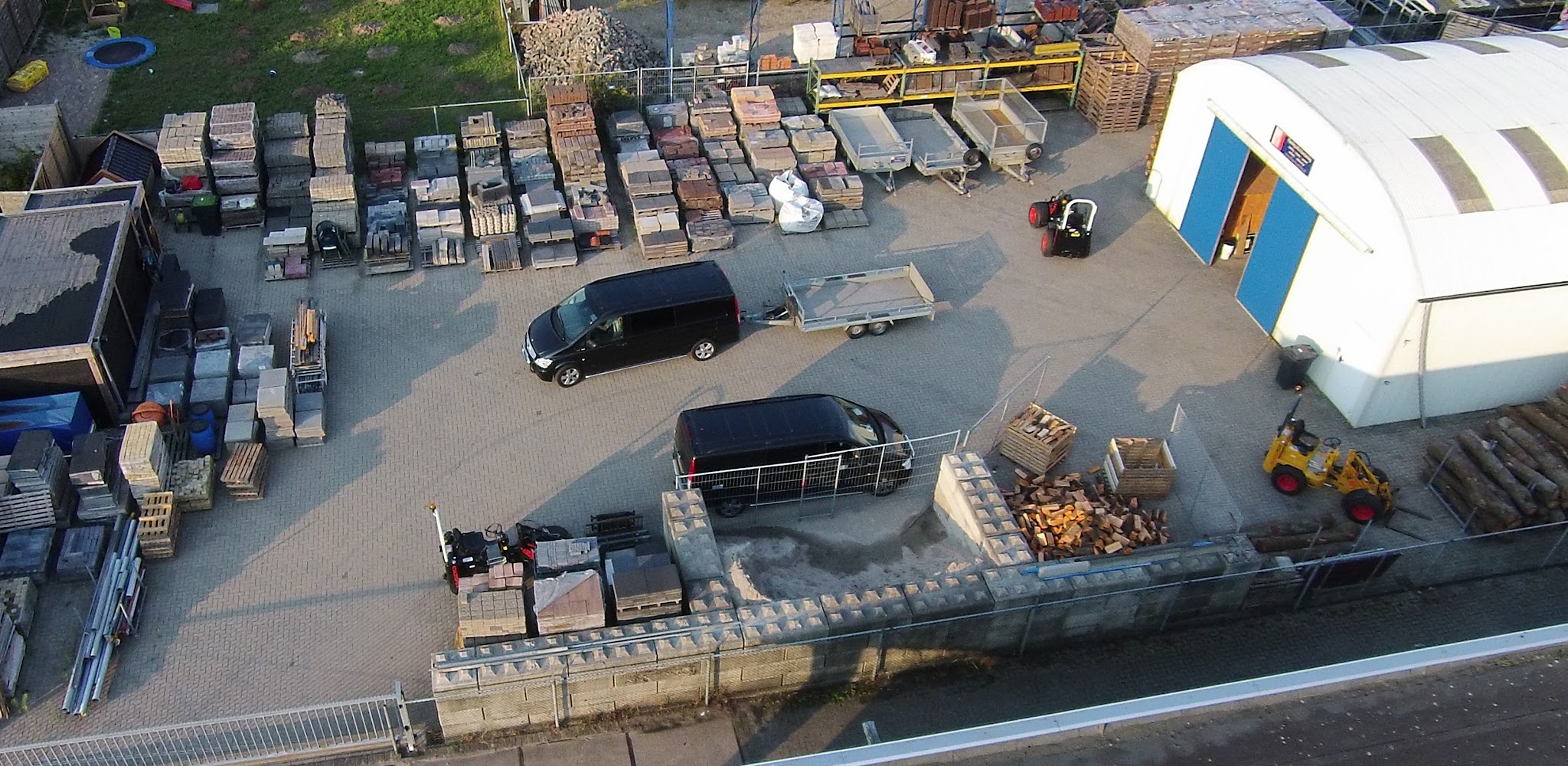 Luchtfoto van het terrein van Fleming Infra Voorziening in Elburg met pallets tegels, aanhangers en de loods