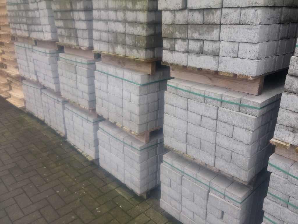 Gestapelde pallets met grijze betonklinkers, omsnoerd met banden